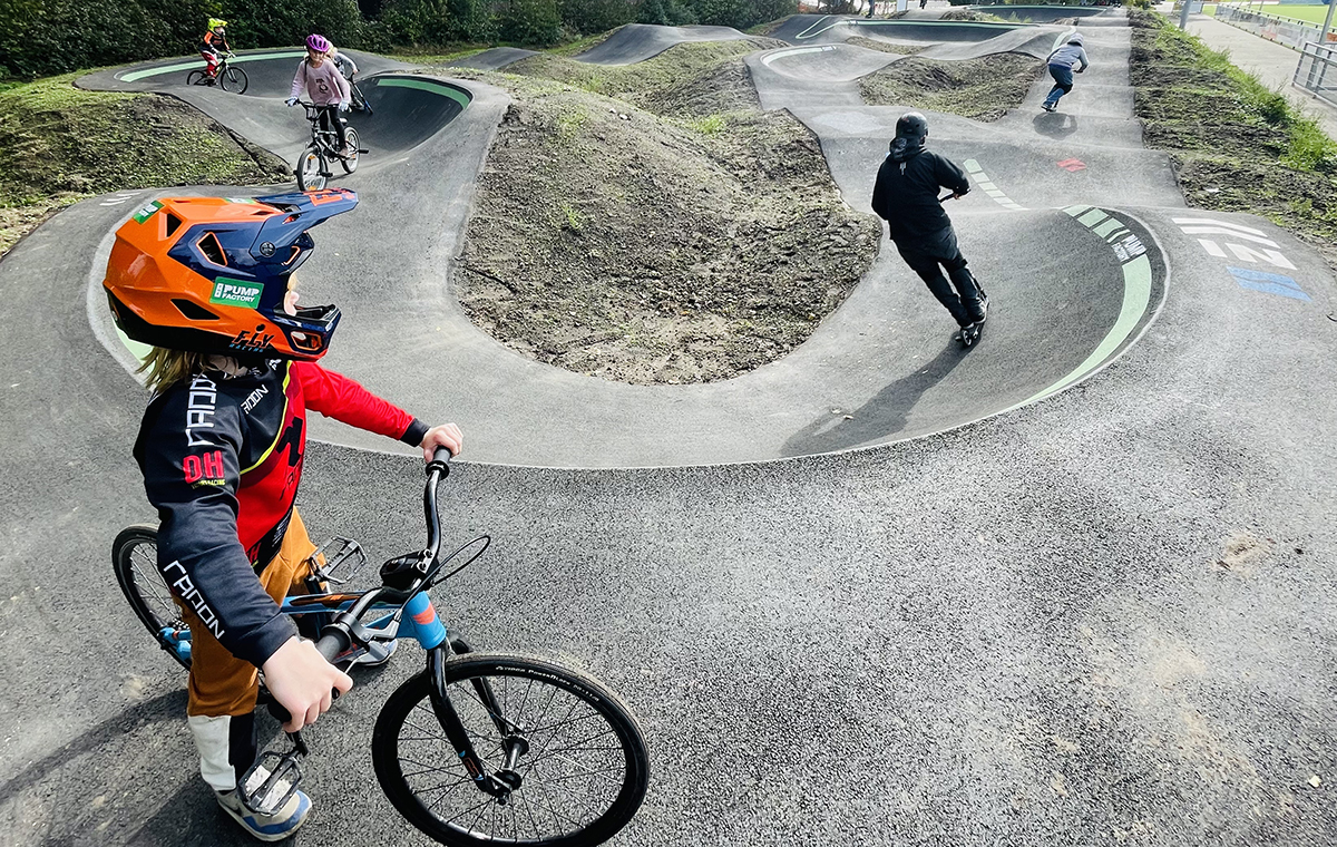 Kinderen met crossfietsen en steps op de speciale geasfalteerde baan met bochten en heuvels.